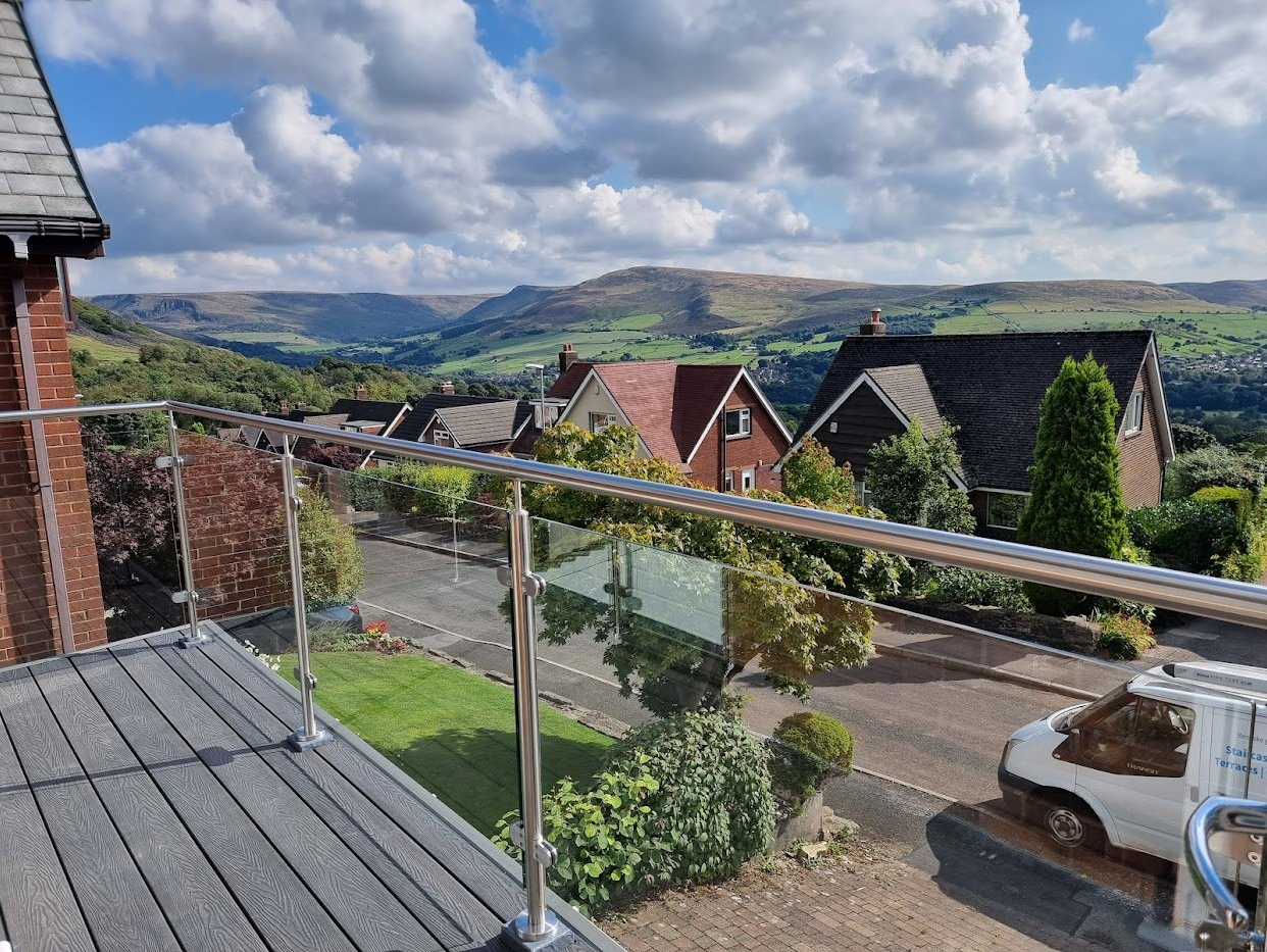 Frameless glass balcony balustrade with a slim handrail, installed by Manchester Balustrades, overlooking open countryside